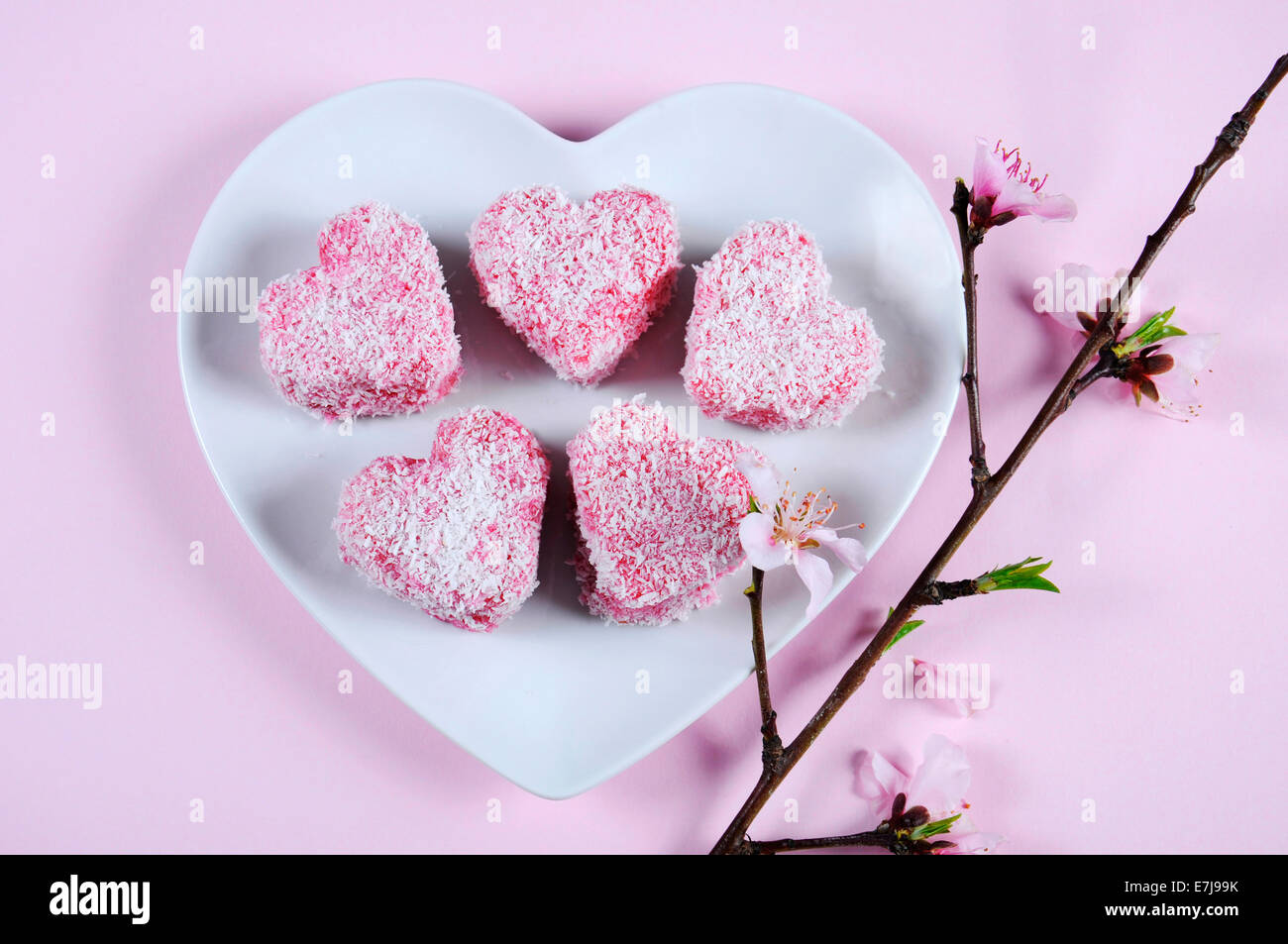 Style australien fait maison en forme de coeur rose petit gâteau Lamington sur plaque blanche en forme de coeur Banque D'Images