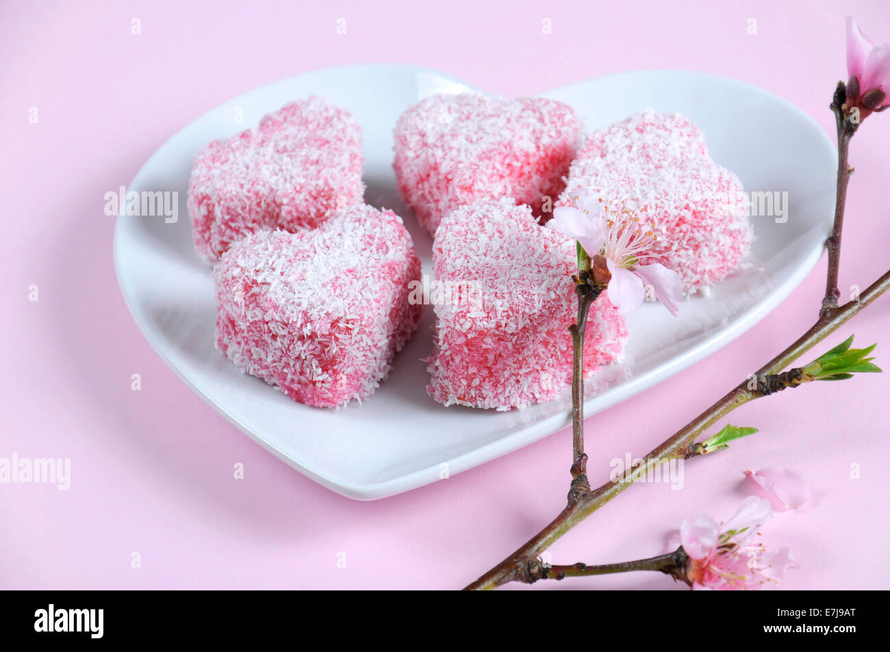 Style australien fait maison en forme de coeur rose petit gâteau Lamington sur plaque blanche en forme de coeur Banque D'Images