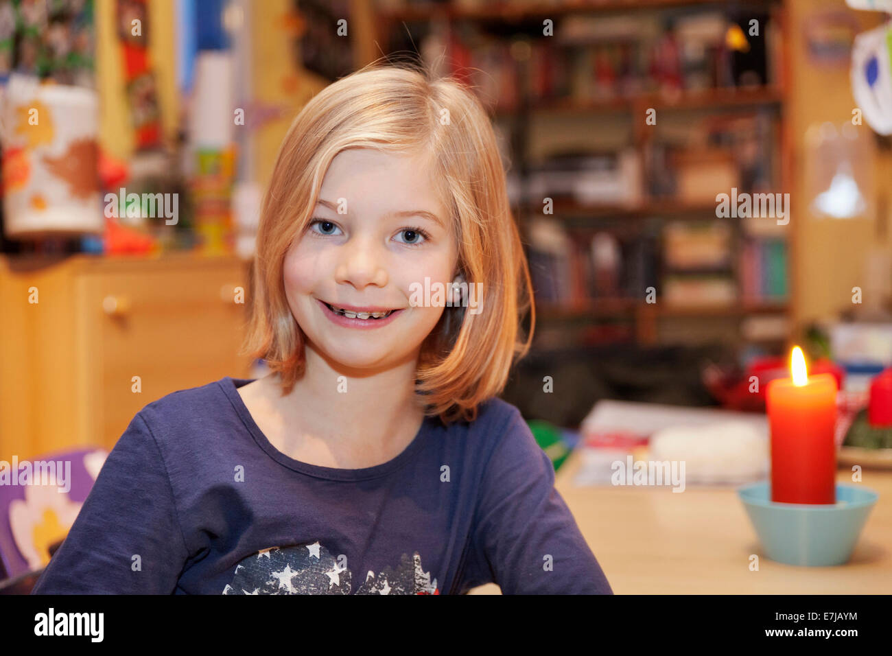 Smiling girl, 9, assis à une table avec une bougie Banque D'Images