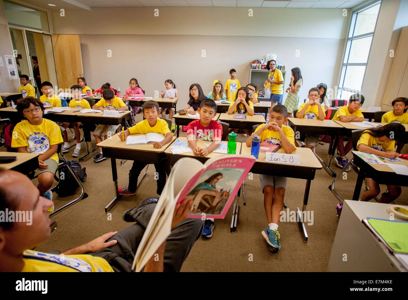 Les élèves de collège multiethnique comme écouter un enseignant lit 'les voyages de Gulliver' à haute voix à un atelier d'apprentissage d'été à Irvine, CA. Remarque T shirts jaune. Banque D'Images