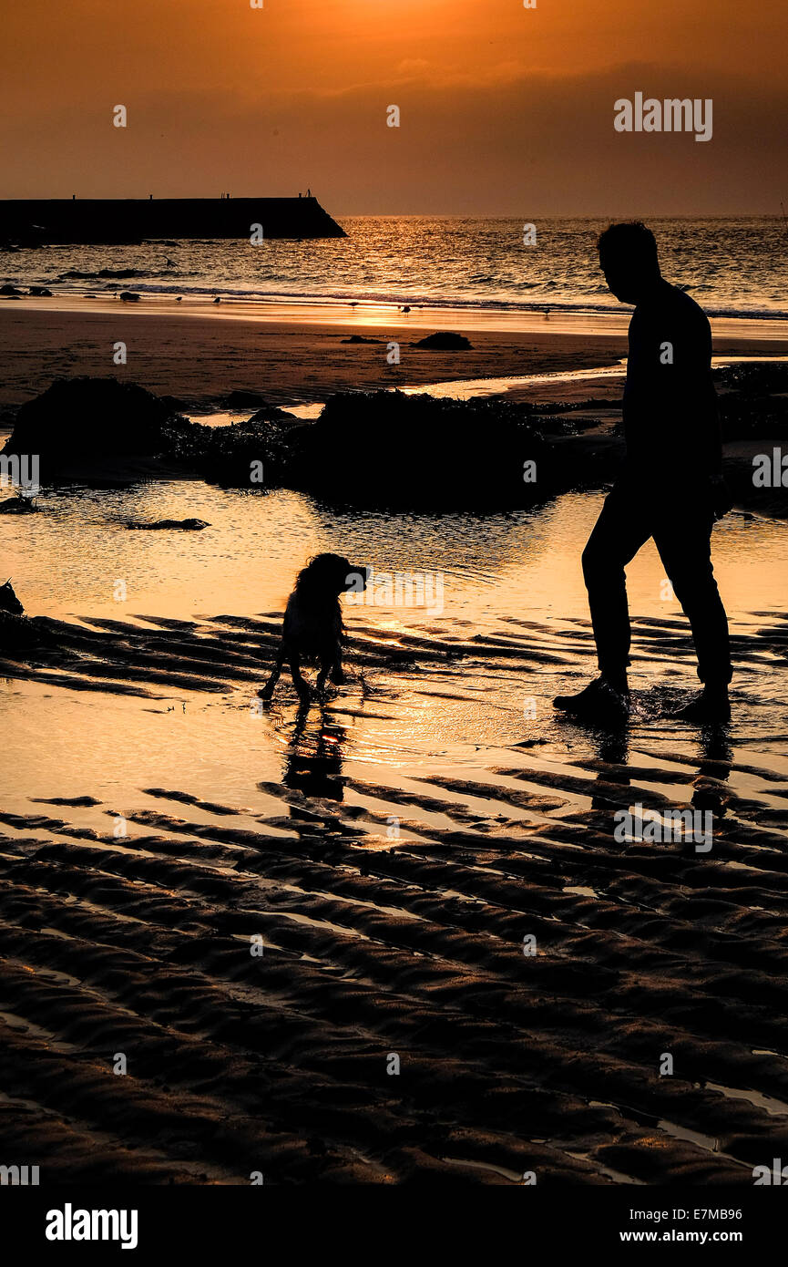 La silhouette d'un homme et son chien sur la plage de Sennen Cove comme le coucher du soleil. Banque D'Images