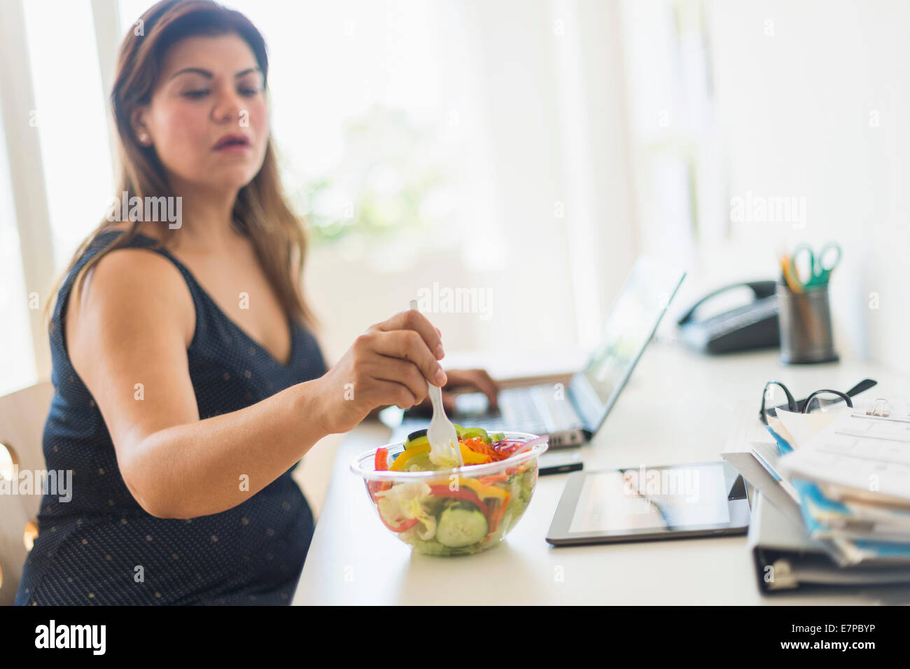 Woman eating salad and using laptop in office Banque D'Images