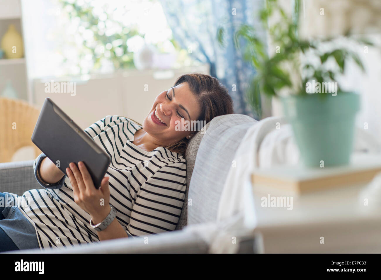 Portrait of happy woman lying on sofa with tablet pc Banque D'Images