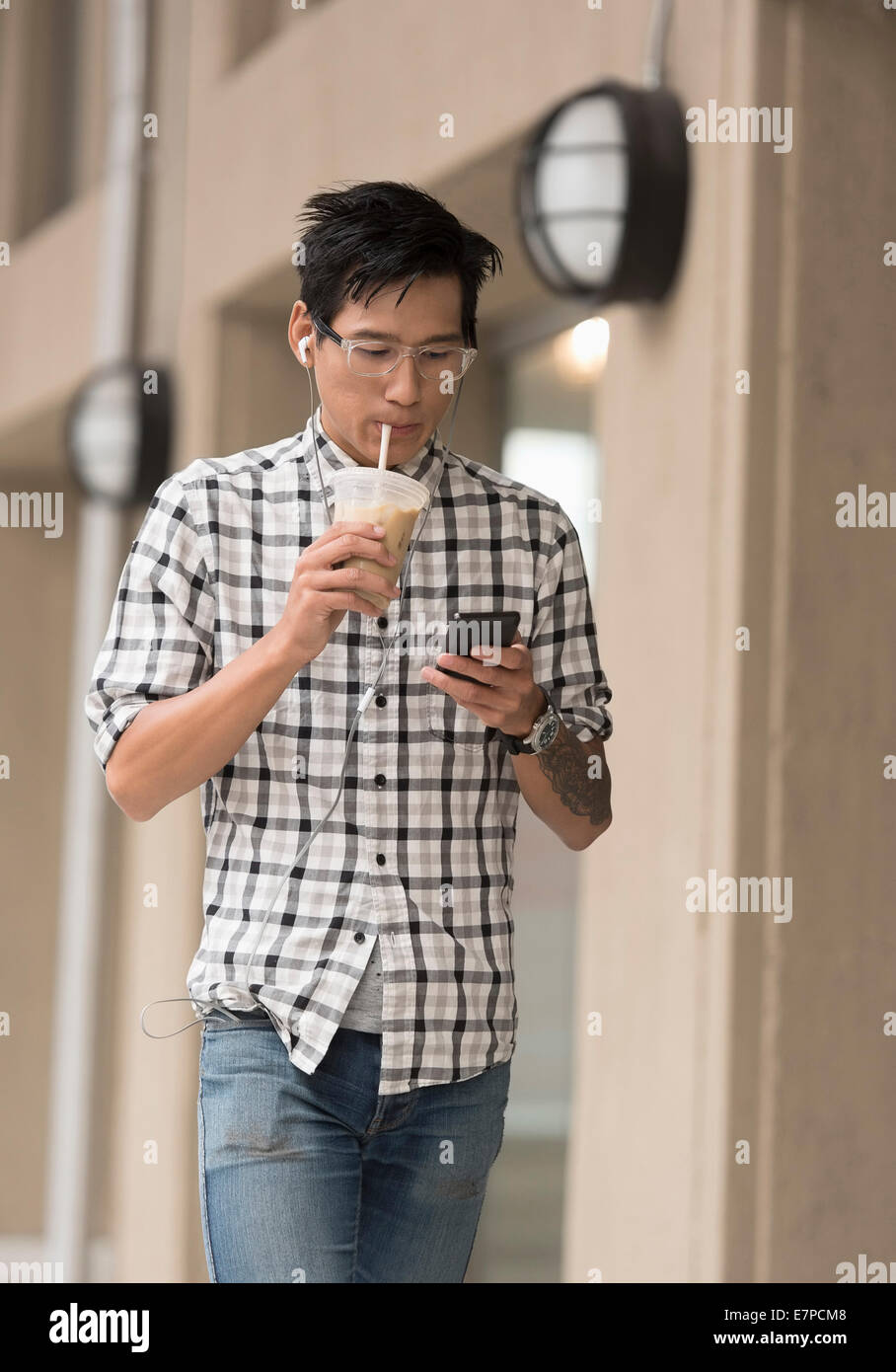 Homme marchant sur un trottoir avec un café glacé et d'un téléphone mobile Banque D'Images