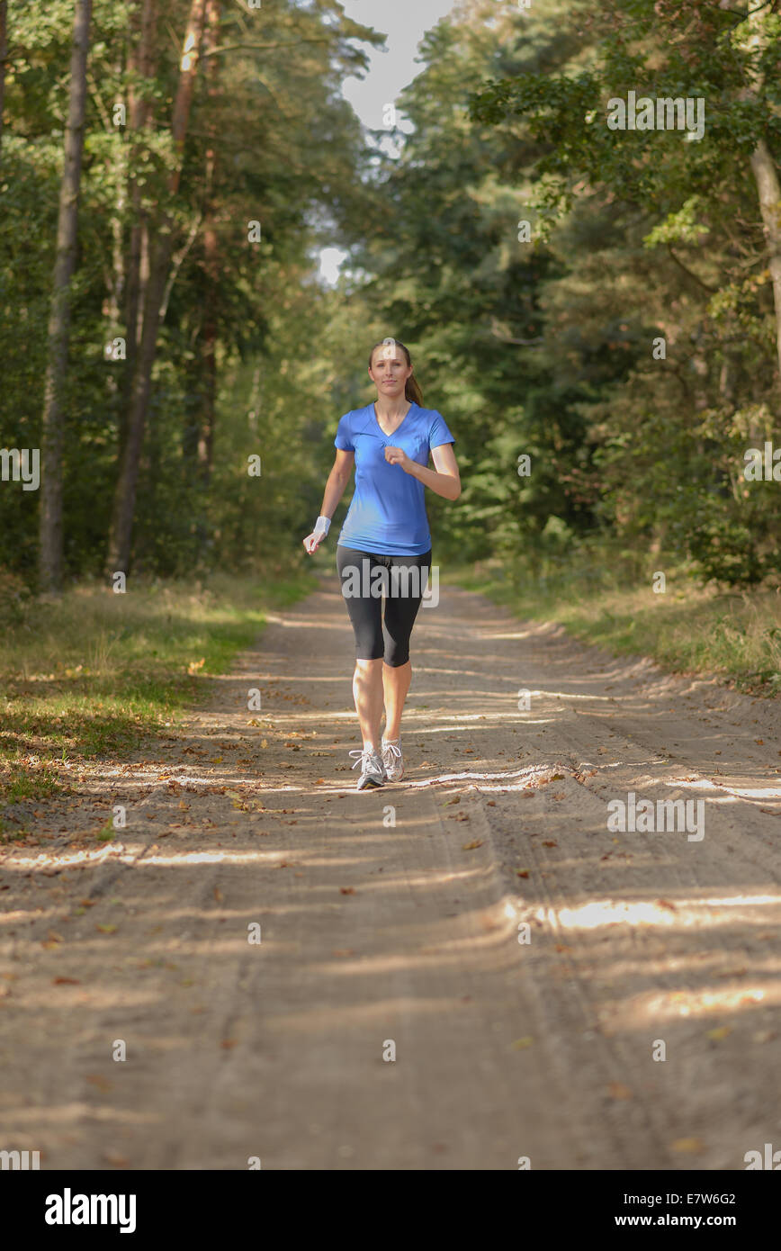 Athletic femme sur le jogging dans une forêt près de la caméra le long d'un chemin à travers les arbres dans un conce santé et fitness Banque D'Images