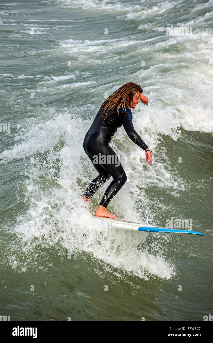 Surfer avec des dreadlocks en noir bottines équitation sur des vagues de surf comme il casse le long de la côte de la mer du Nord Banque D'Images