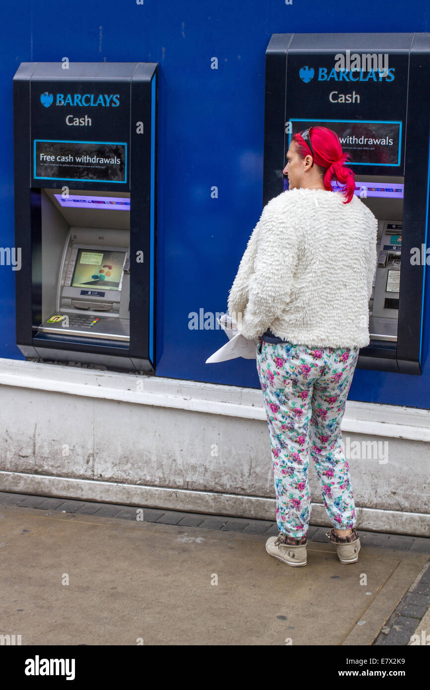 Une jeune femme aux cheveux rouges un ATM Barclays Cash machine Banque D'Images