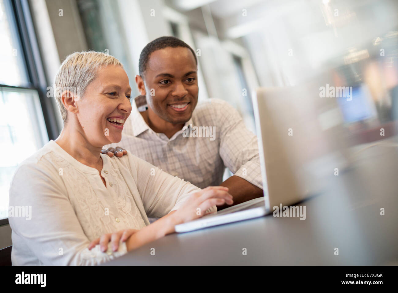 La vie de bureau. Deux personnes, un homme et une femme à la recherche d'un écran d'ordinateur portable et de rire. Banque D'Images