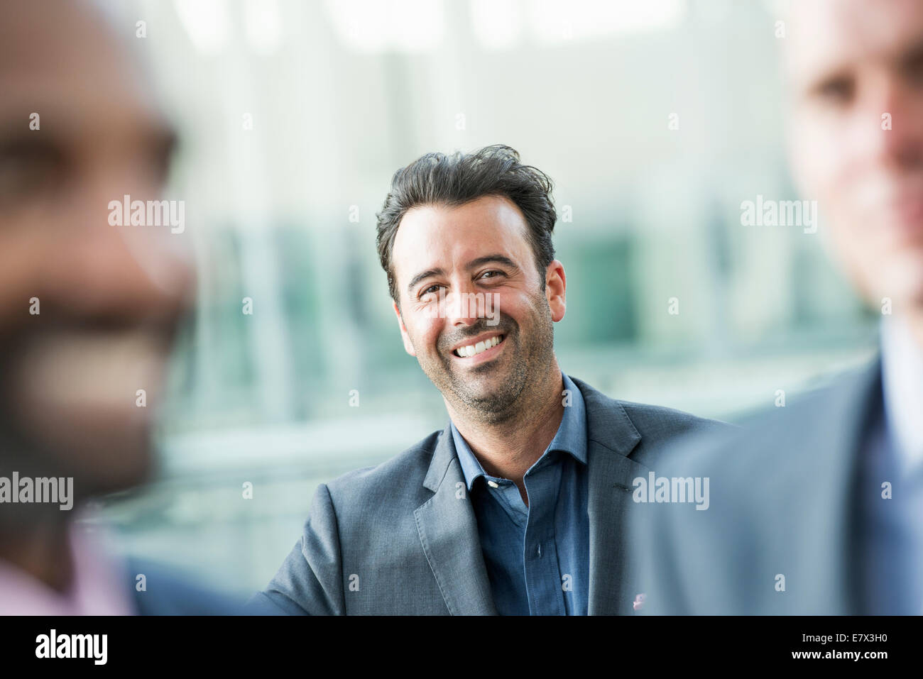 Trois hommes d'affaires, l'un souriant à la caméra, à la recherche entre les deux autres. Banque D'Images