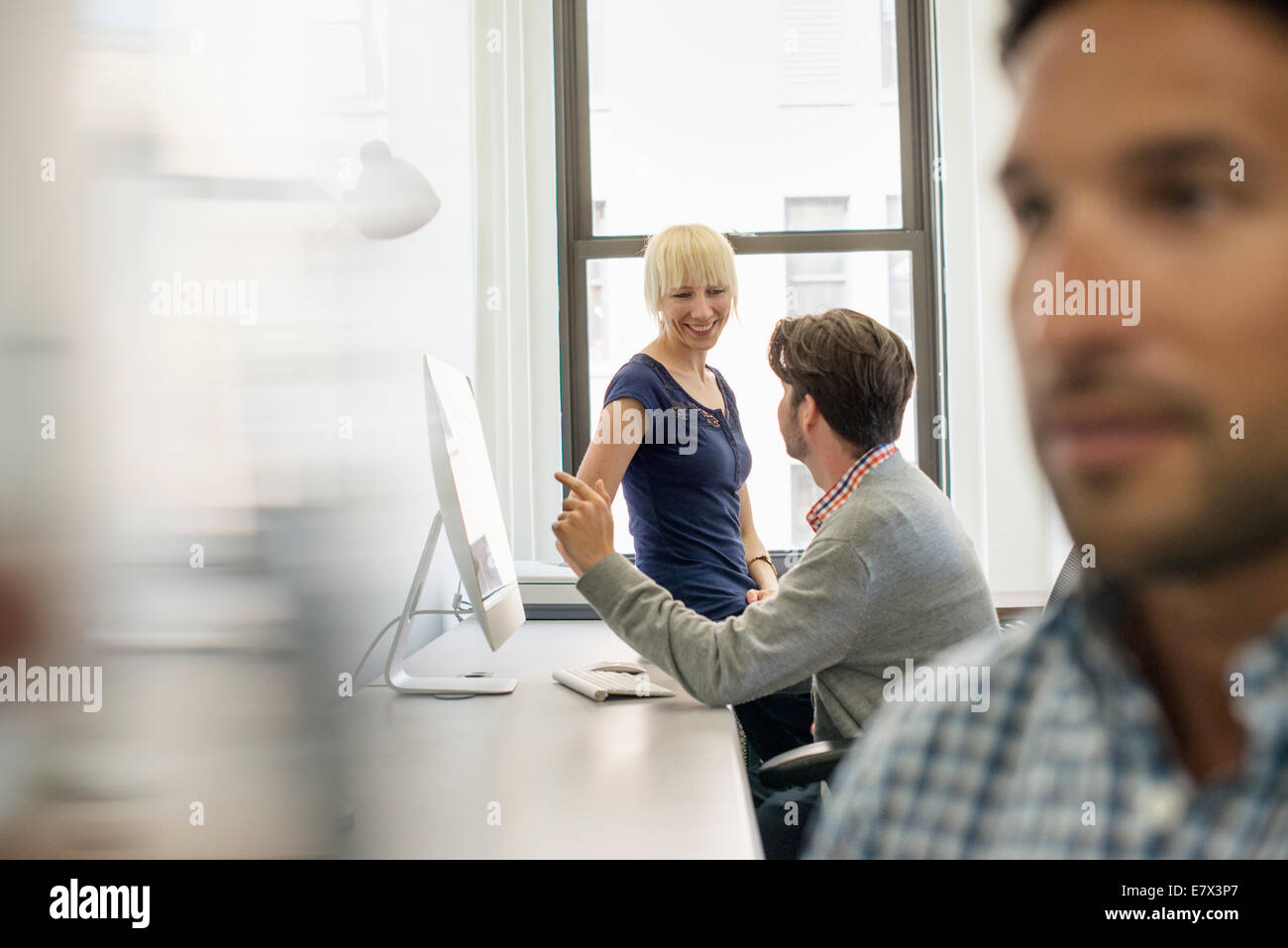 Trois collègues d'affaires dans un bureau, deux de parler et l'un debout près de la porte à l'écoute. Banque D'Images