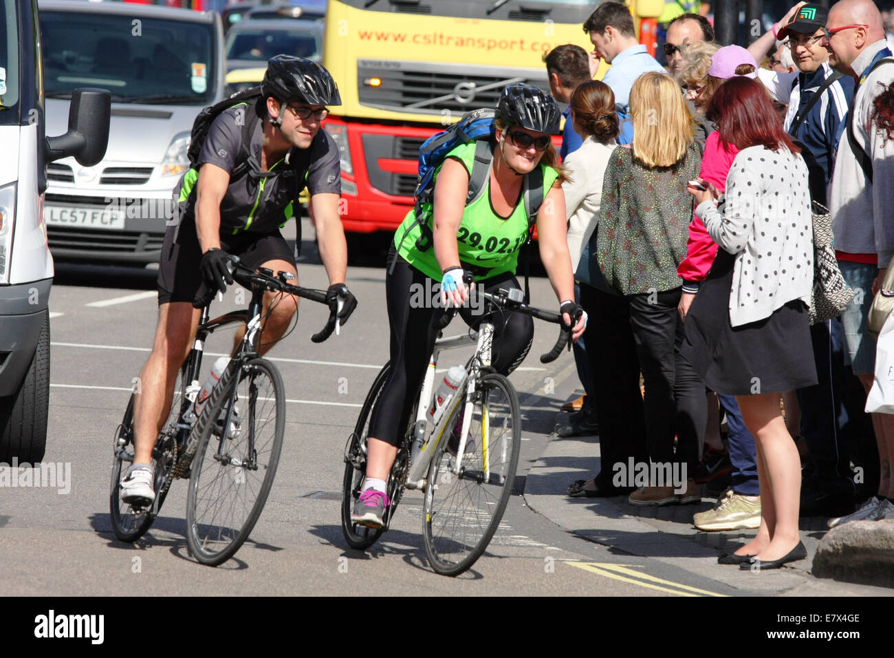 Deux cyclistes équitation autour d'un coin de Londres que les piétons attendent pour traverser la route Banque D'Images