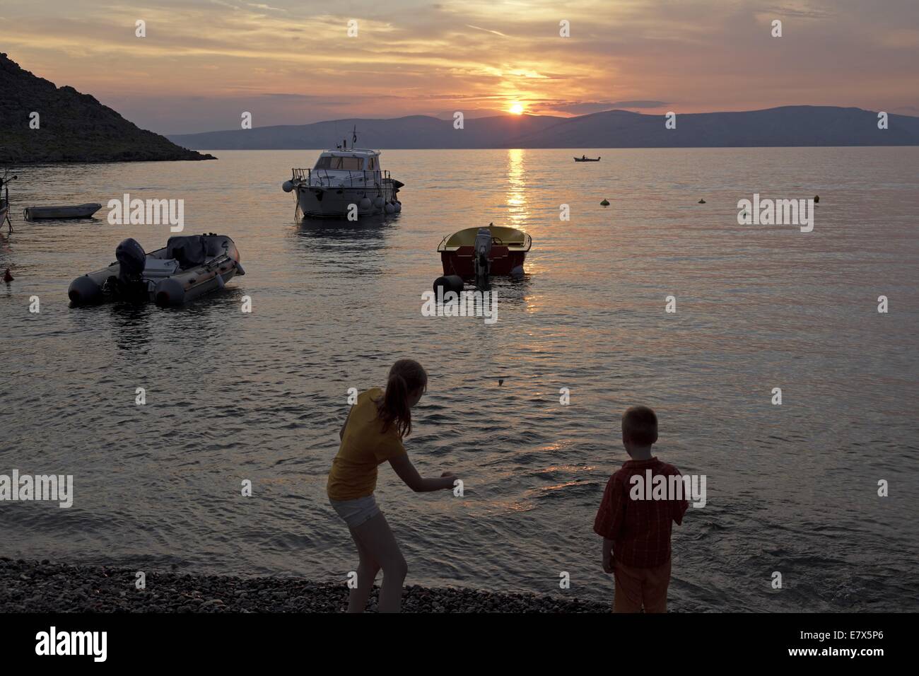 Boy and girl skipping rocks pendant le coucher du soleil au bord de la mer, Labin, golfe de Kvarner, Croatie Banque D'Images