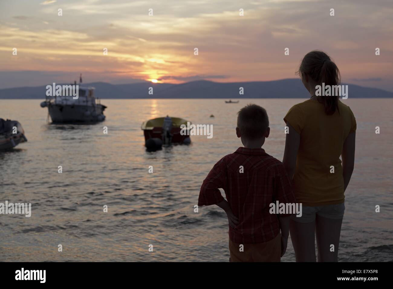 Garçon et fille à regarder le coucher du soleil au bord de la mer, Labin, golfe de Kvarner, Croatie Banque D'Images