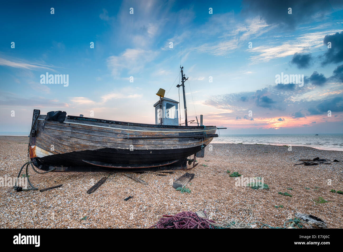 Un vieux bateau en bois sur une plage de galets au lever du soleil Banque D'Images
