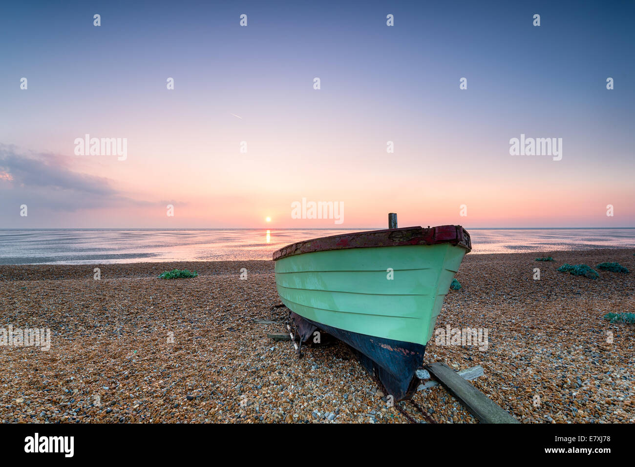 Beau lever de soleil sur un bateau de pêche en bois vert sur une plage déserte Banque D'Images