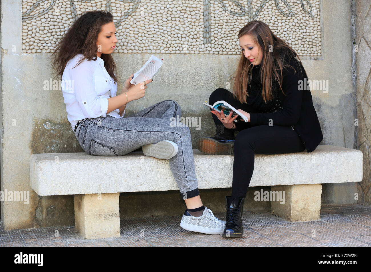 Deux copines, adolescents, assis sur un banc en pierre, la lecture de livres, Menton, Alpes-Maritimes, Provence Alpes, France Banque D'Images