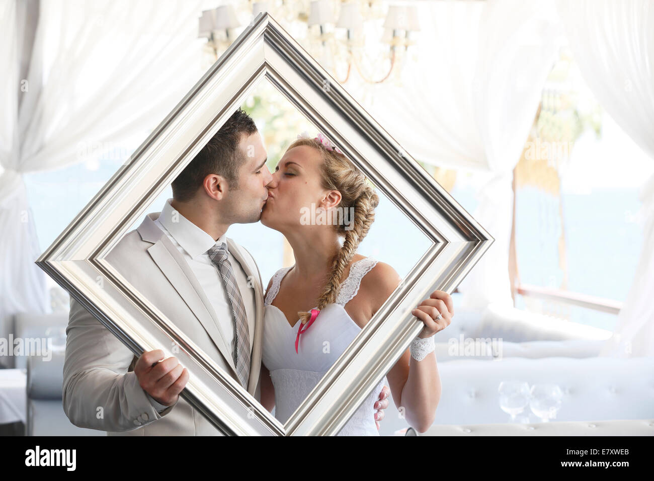 Bride and Groom holding un cadre photo en face d'eux, s'embrasser, pousse de photo Banque D'Images