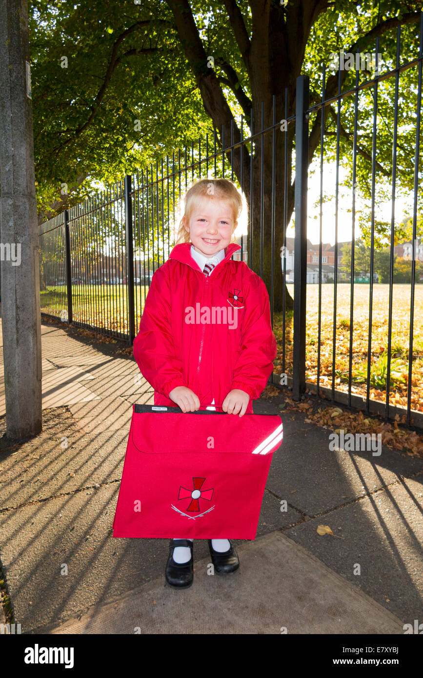 Un enfant de 4 ans / fille dans son nouvel uniforme rouge aller à / sur le chemin de sa classe d'accueil à l'enfant de l'État l'école primaire. UK. Banque D'Images