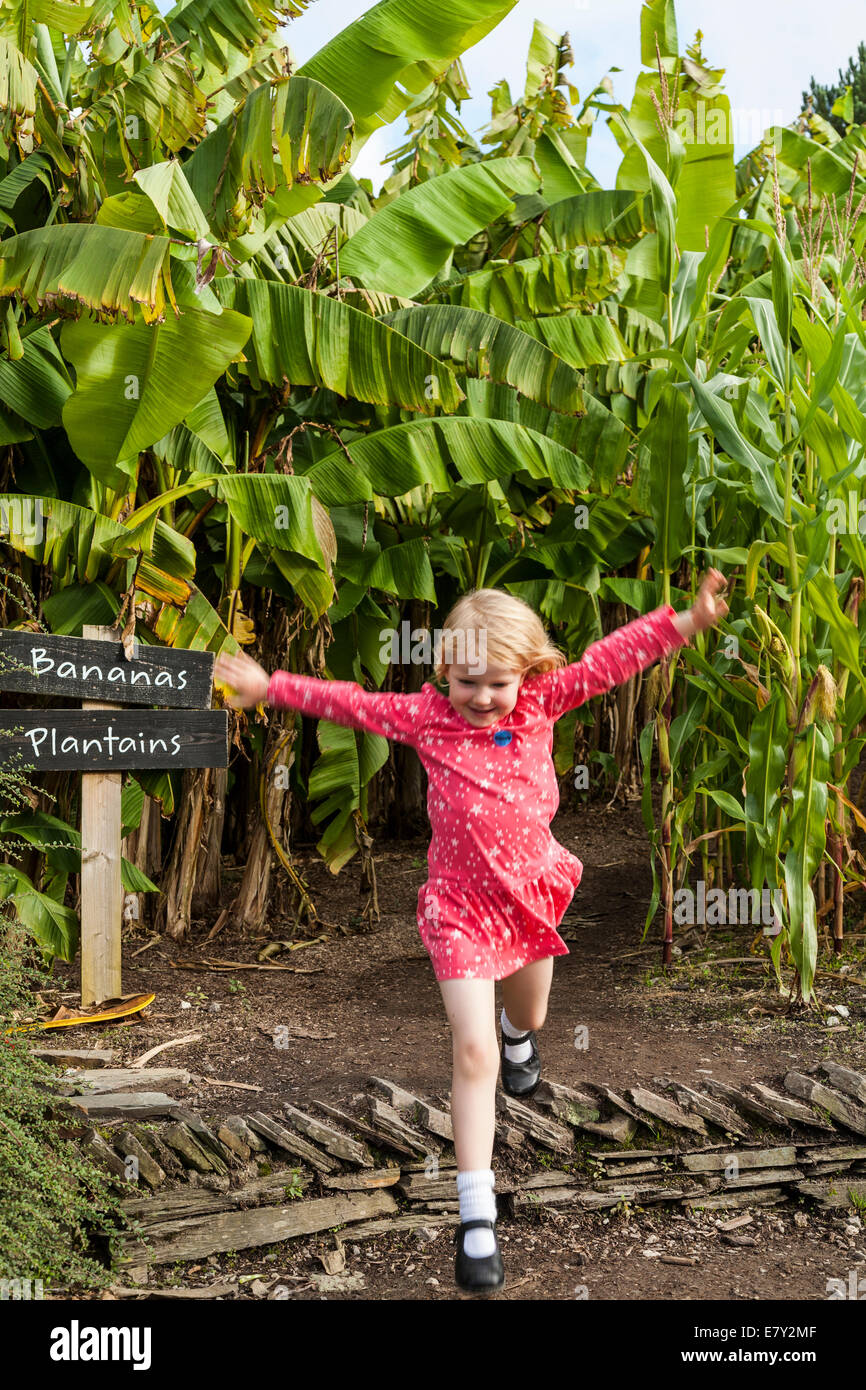 4 quatre ans, fille / enfant marche et lecture / jump / sautant dans l'Eden Project, à l'extérieur jardin extérieur. Cornwall. UK. Banque D'Images