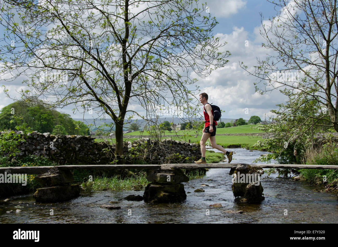 L'homme en jogging de sport en pierre historique passage clapper pont sur Austwick Beck dans le magnifique paysage de la campagne, - du Yorkshire, England, UK. Banque D'Images