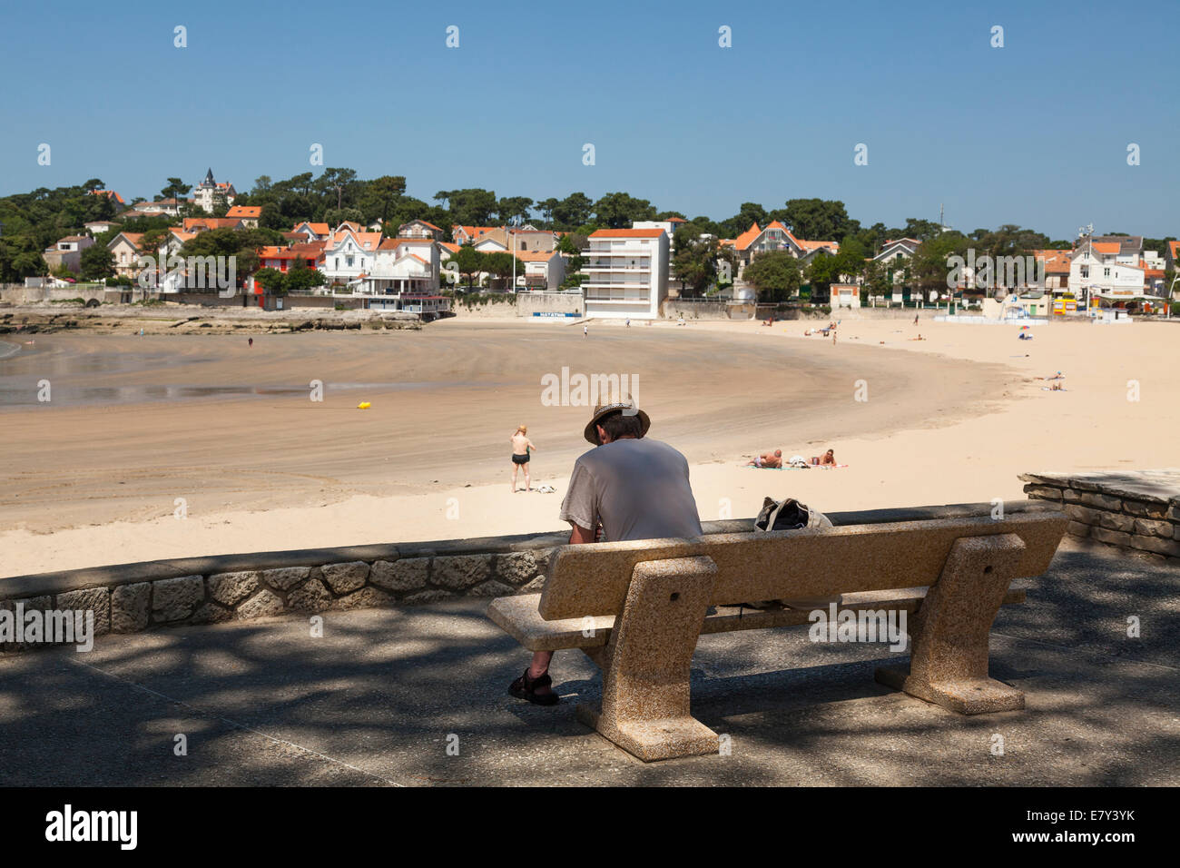 Homme assis sur un banc ombragé donnant sur la lecture de la plage d'adresses. Banque D'Images