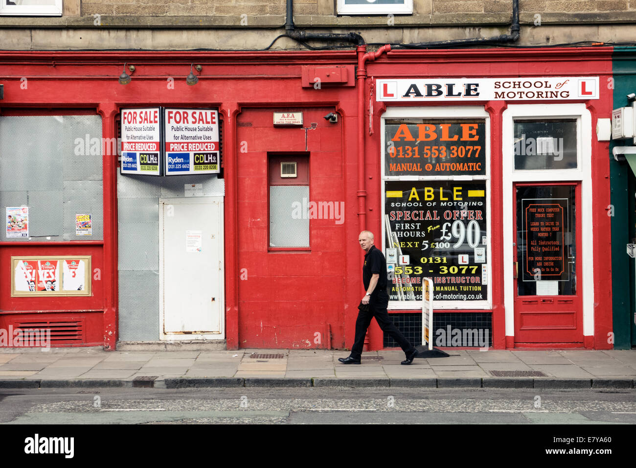Homme marchant passé une école de conduite automobile et des petites entreprises un barricadèrent shop à Leith, Édimbourg Banque D'Images