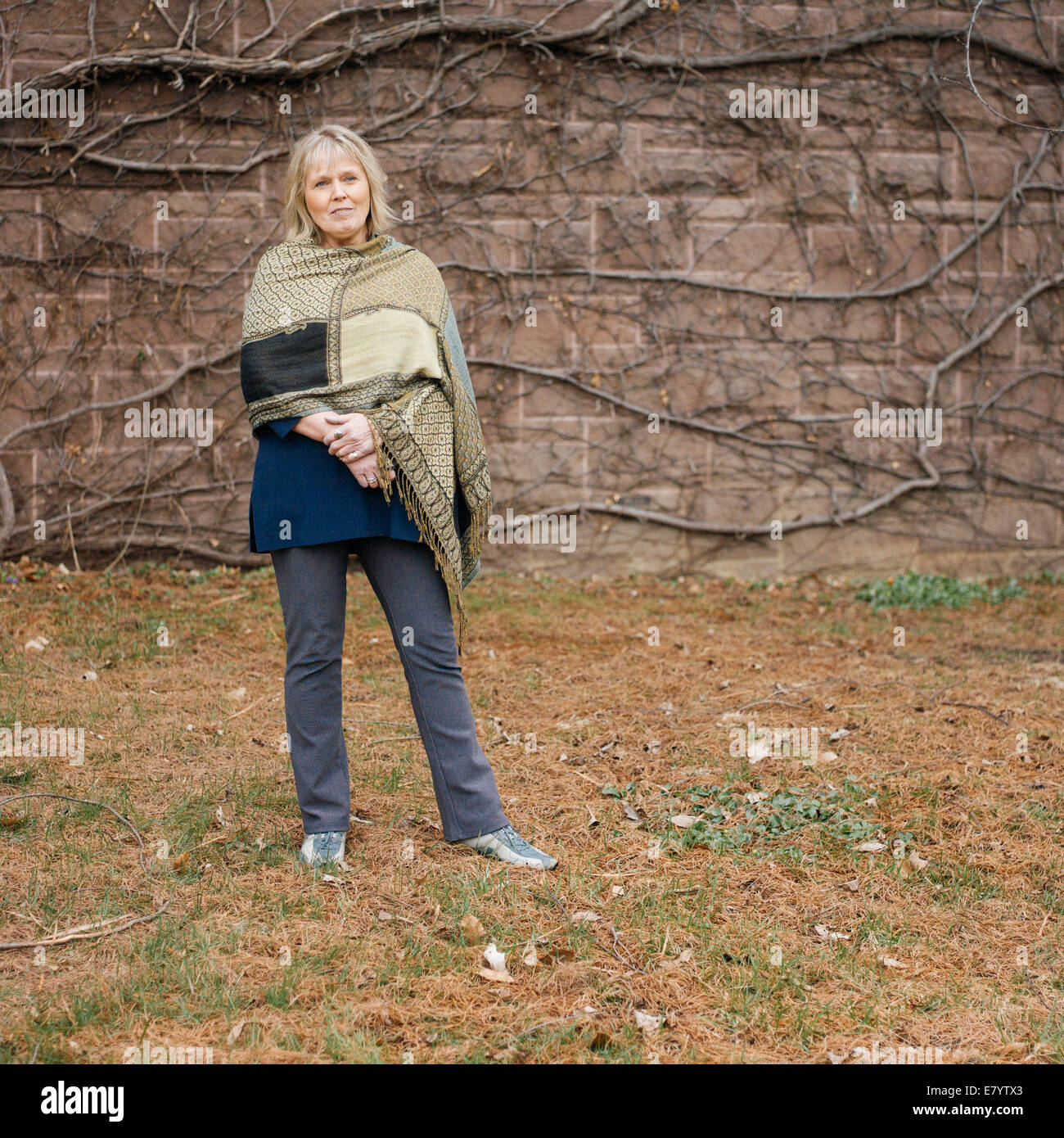 Senior woman standing contre mur recouvert de lierre sans feuilles Banque D'Images