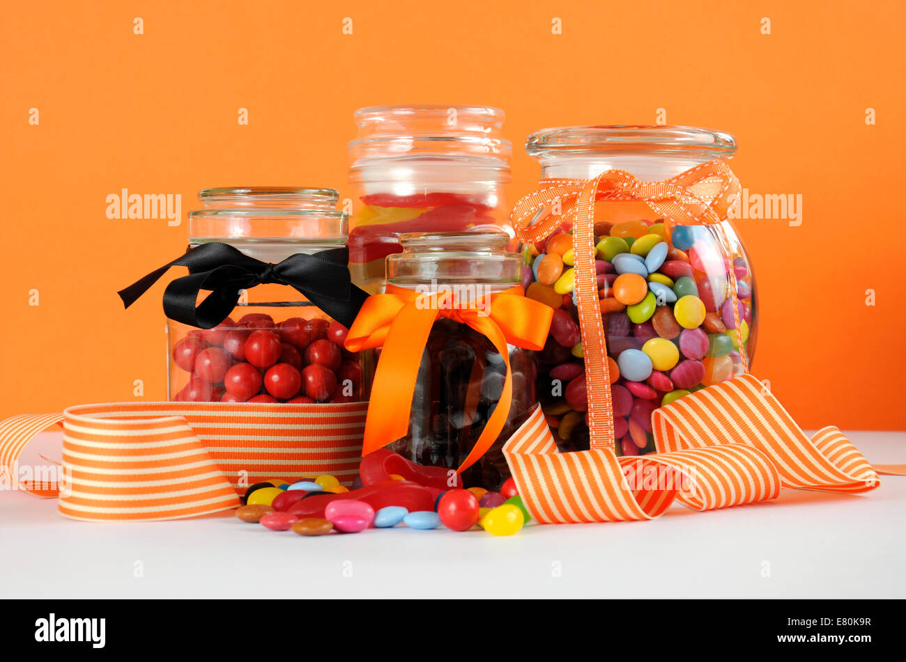 Des bonbons dans des bocaux en verre avec orange et blanc ruban bande pour l'Halloween ou des faveurs de partie. Banque D'Images