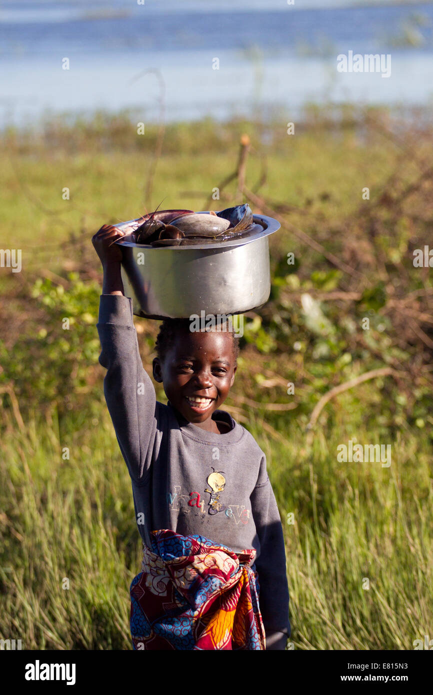 Un jeune enfant porte un seau de poissons dans un village de pêche dans les zones humides, la Zambie Bangweulu Banque D'Images