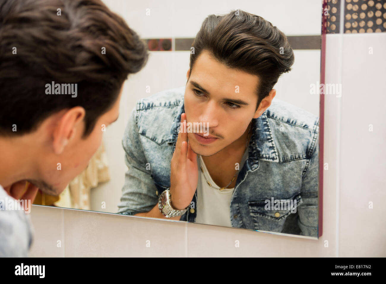 Beau jeune homme, examinant son visage peau de près, dans la salle de bains miroir le matin Banque D'Images