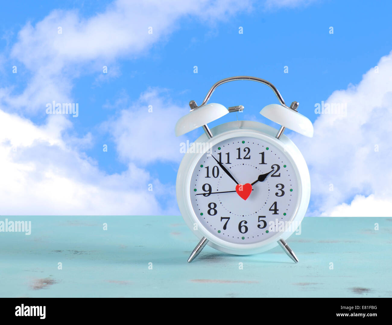L'heure d'horloge blanc sur une table en bois vintage aqua bleu contre un ciel avec nuages de fond. Banque D'Images