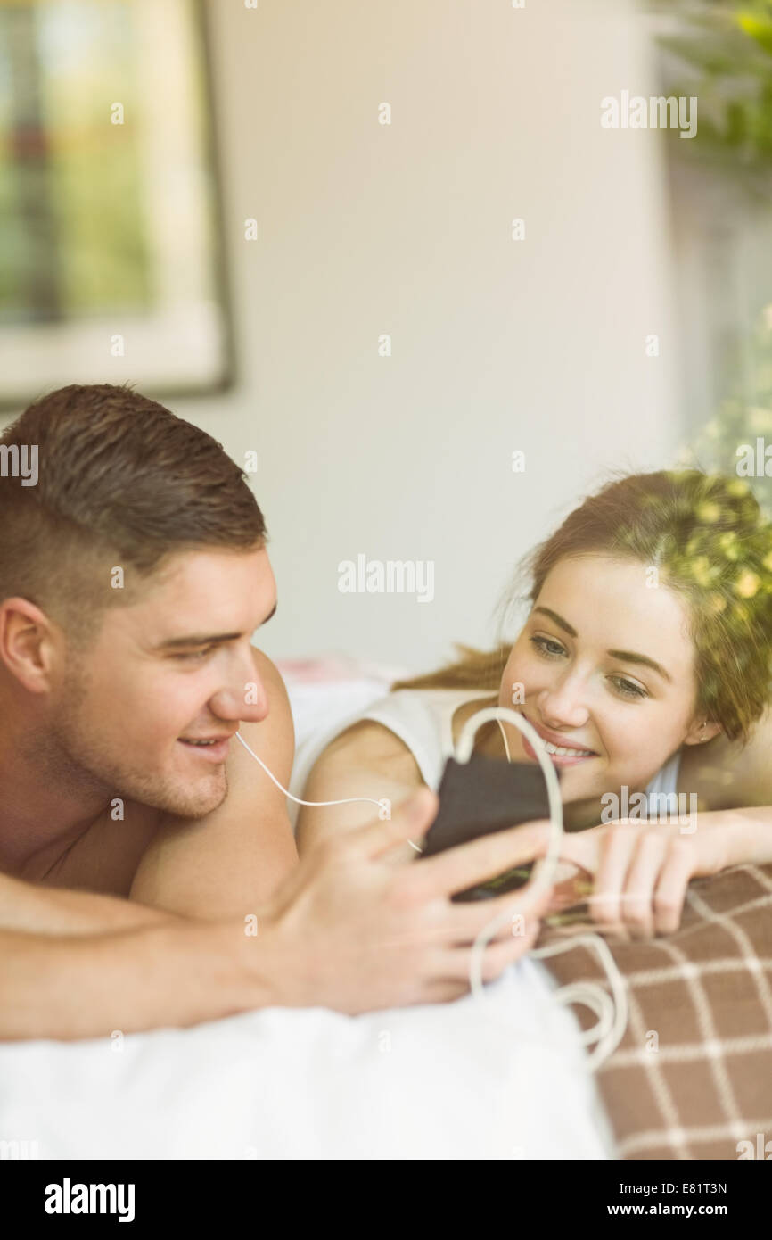 Cute couple lying on bed listening to music Banque D'Images