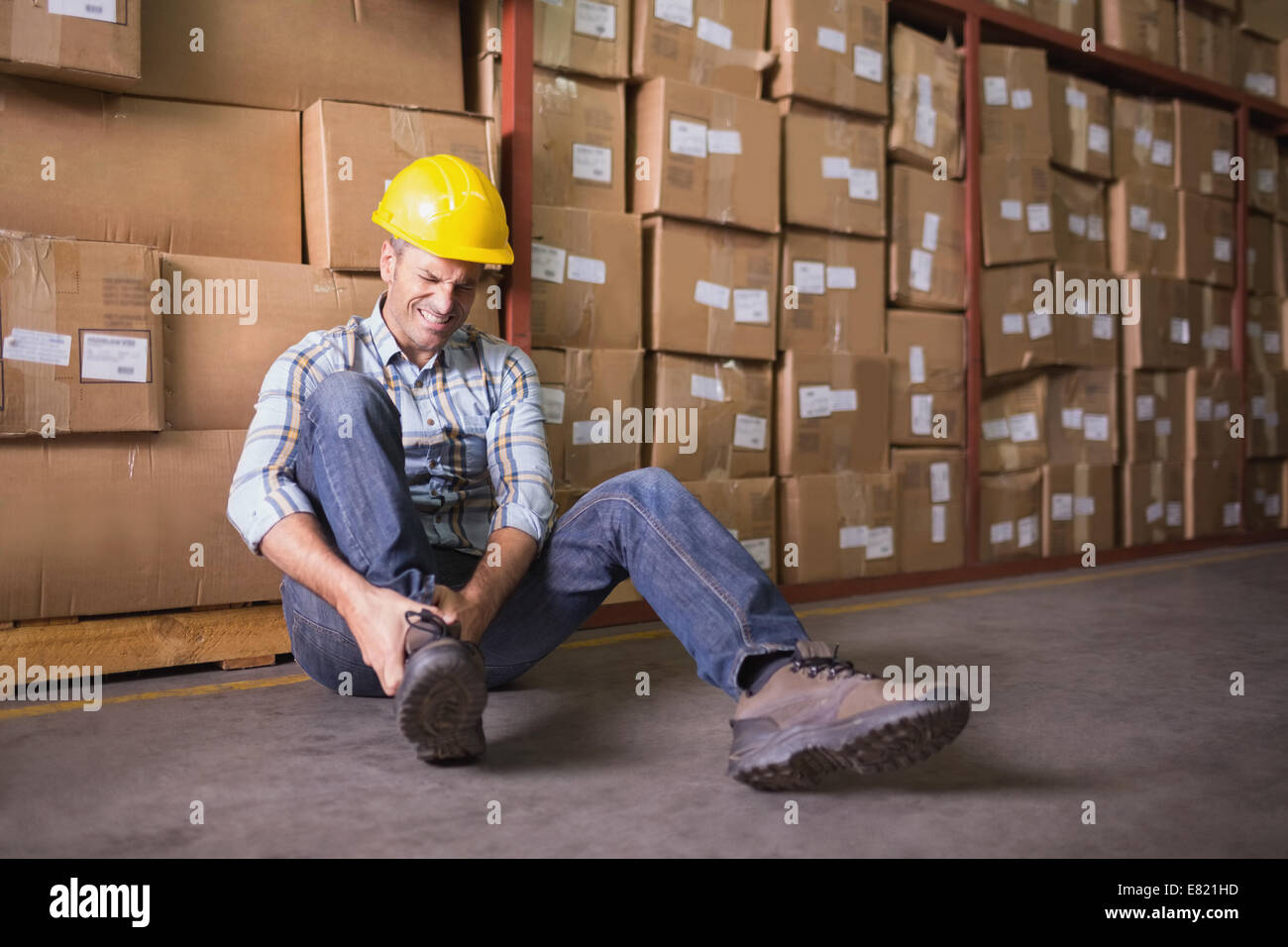 Travailleur avec l'entorse de la cheville sur le plancher de l'entrepôt Banque D'Images