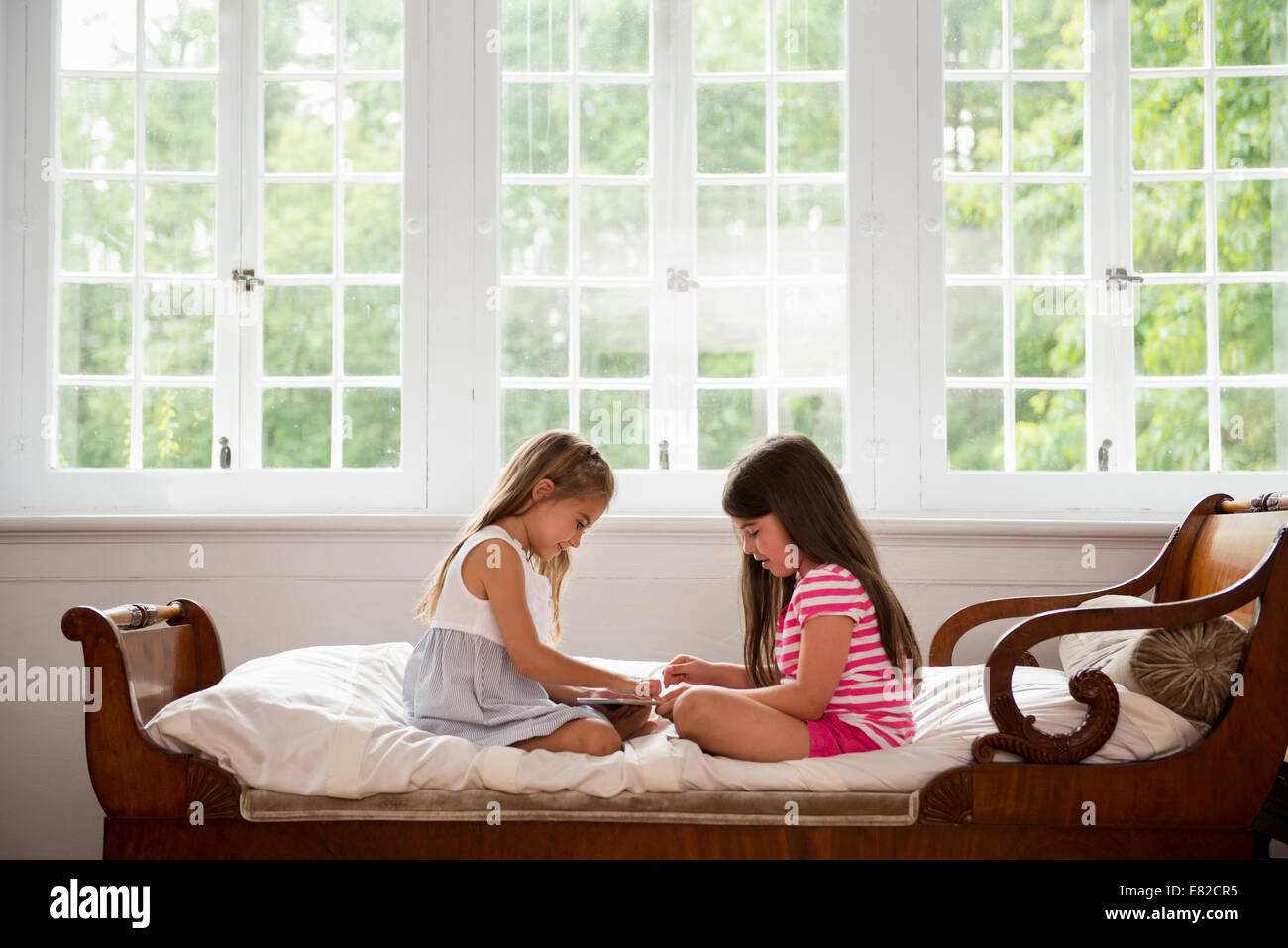 Deux filles assis et de jouer, à l'aide d'une tablette numérique. Banque D'Images