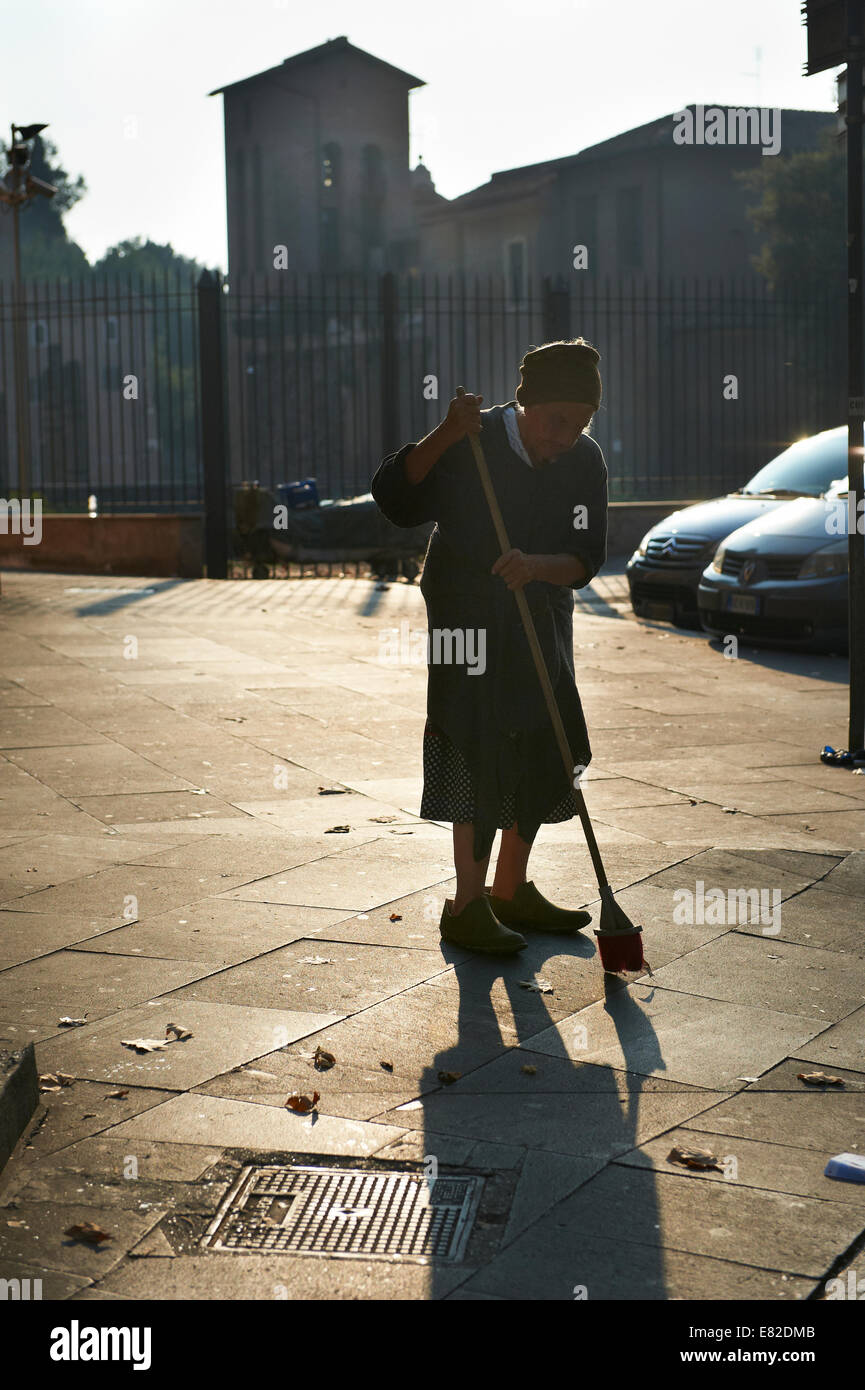 Vieille Femme balayant le trottoir dans le soleil du matin à Rome, Italie Banque D'Images