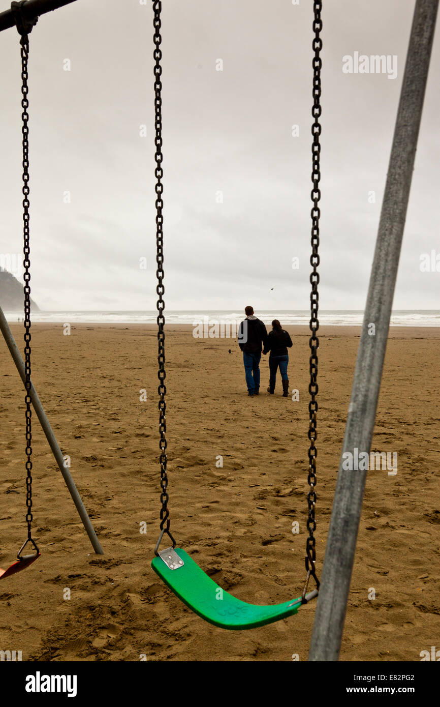 Un couple marche par balançoires vides sur la plage à Seaside, Oregon Banque D'Images