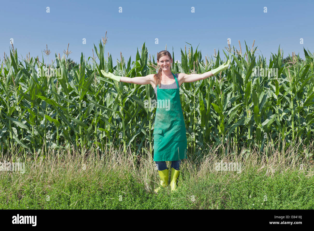 Jeune femme en vêtements de travail debout avec les bras tendus en avant d'un champ de maïs, Bade-Wurtemberg, Allemagne Banque D'Images