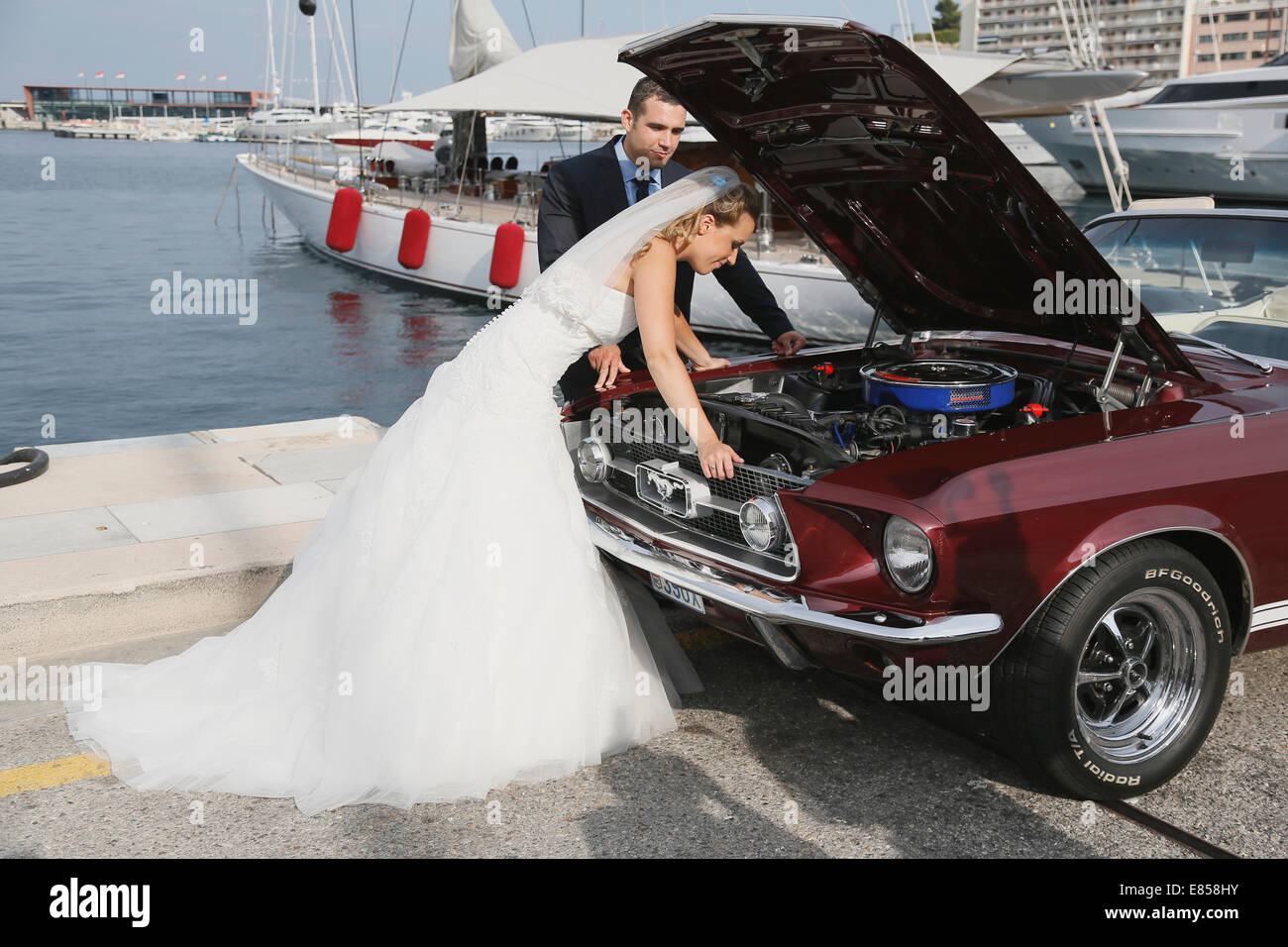 Mariée et le marié à la recherche dans le compartiment moteur d'une Ford Mustang après une panne, dans un port Banque D'Images