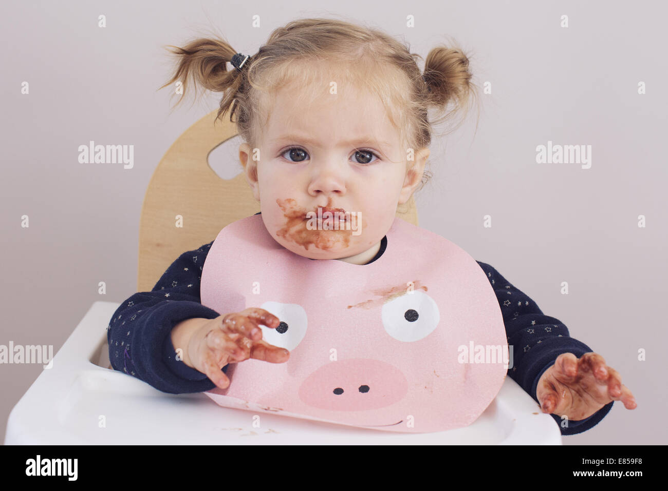 Baby Girl sitting in chaise haute avec la nourriture enduite sur son visage et ses mains Banque D'Images