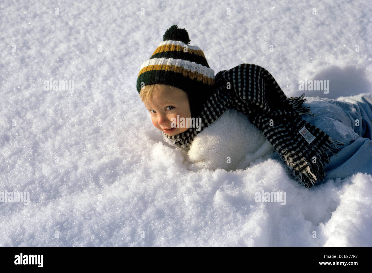 Un heureux quatre-année-vieux garçon de race blanche américaine dans son  bonnet et écharpe en laine et un habit fait un grand sourire après avoir  chuté dans la neige sur une journée ensoleillée