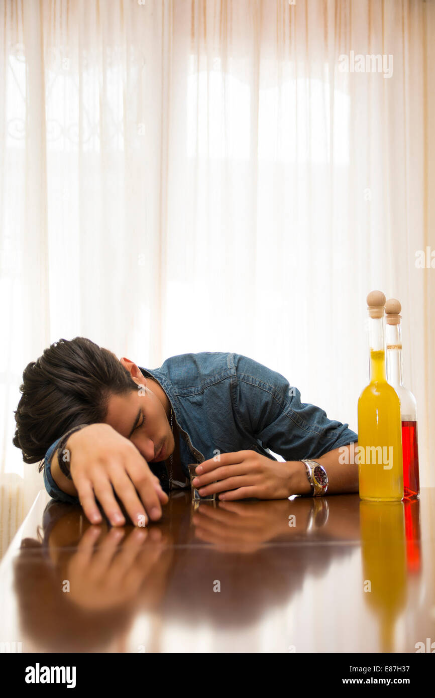 Jeune homme ivre et dormir seul à une table avec deux bouteilles d'alcool à côté de lui en sirotant du verre pour noyer sa Banque D'Images