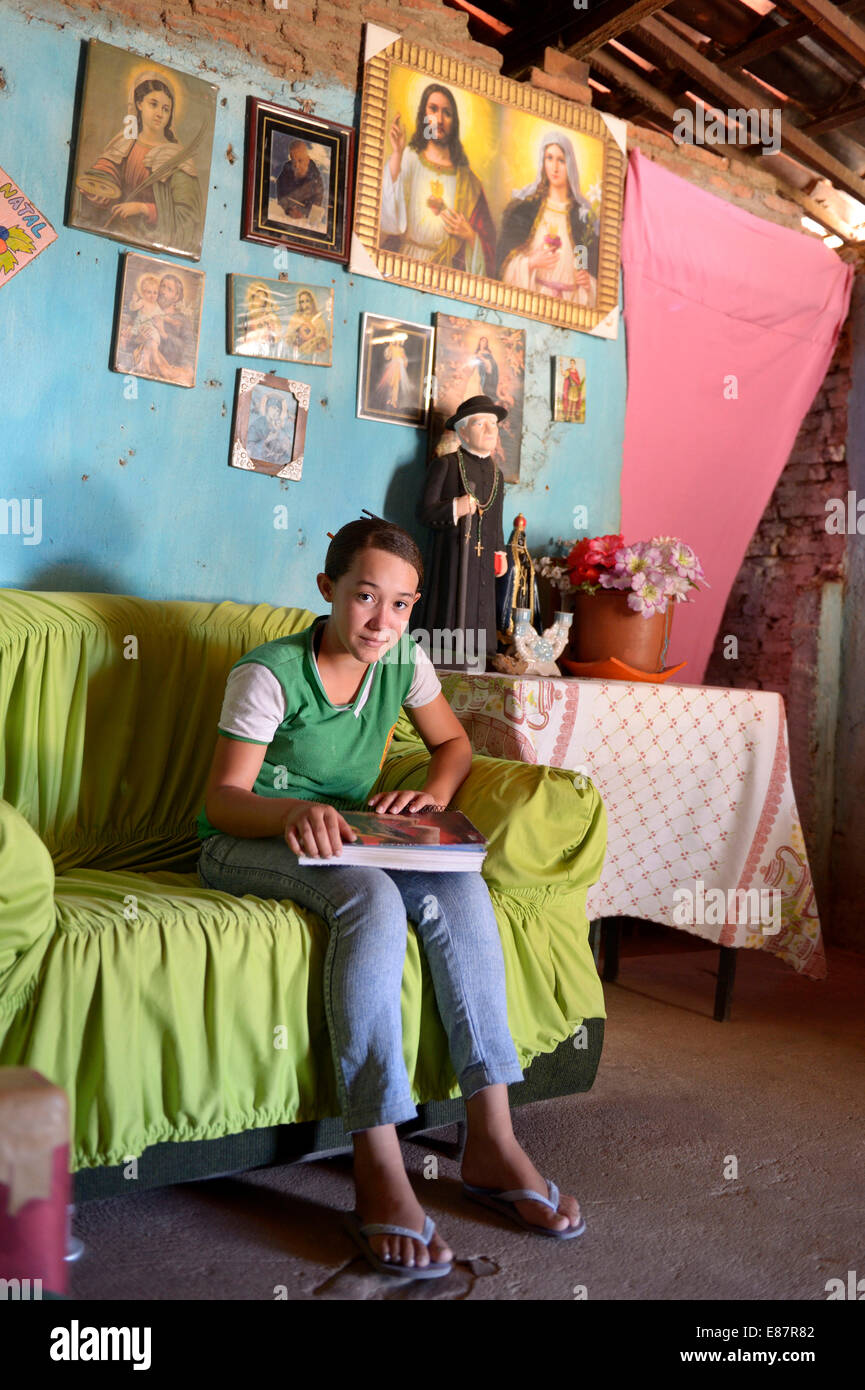 Jeune personne assise dans une simple salle de séjour sous les images des saints, Crato, État de Ceará, Brésil Banque D'Images