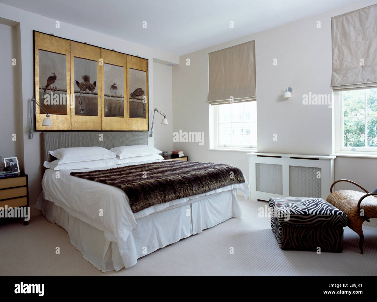 Dorure ancienne encadrée au-dessus de lit avec des panneaux de faux lancer et linge blanc dans une chambre moderne avec abat-jour gris sur windows Banque D'Images