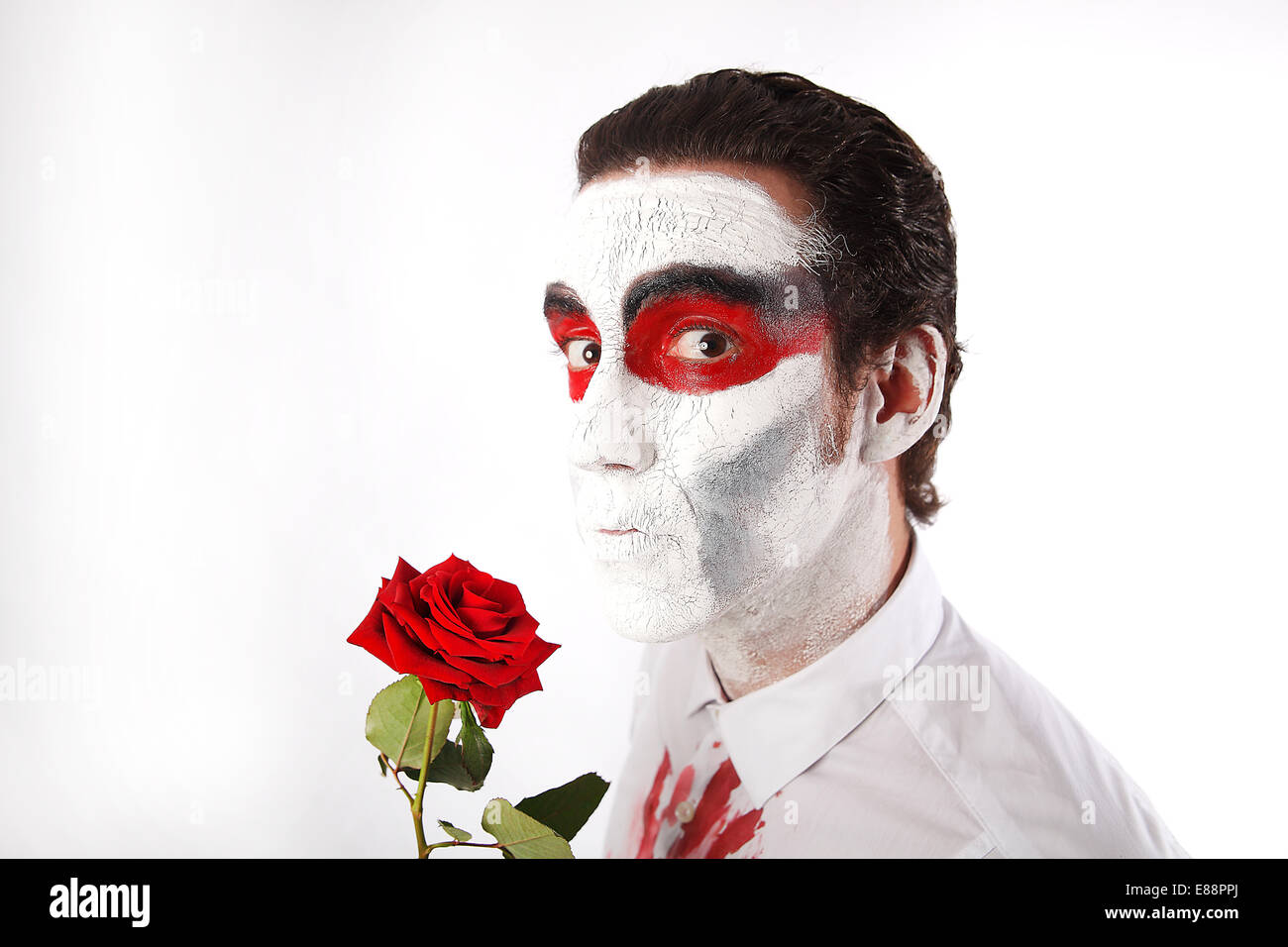 L'homme blanc avec mascara et bloody shirt détient rose rouge devant un fond blanc Banque D'Images