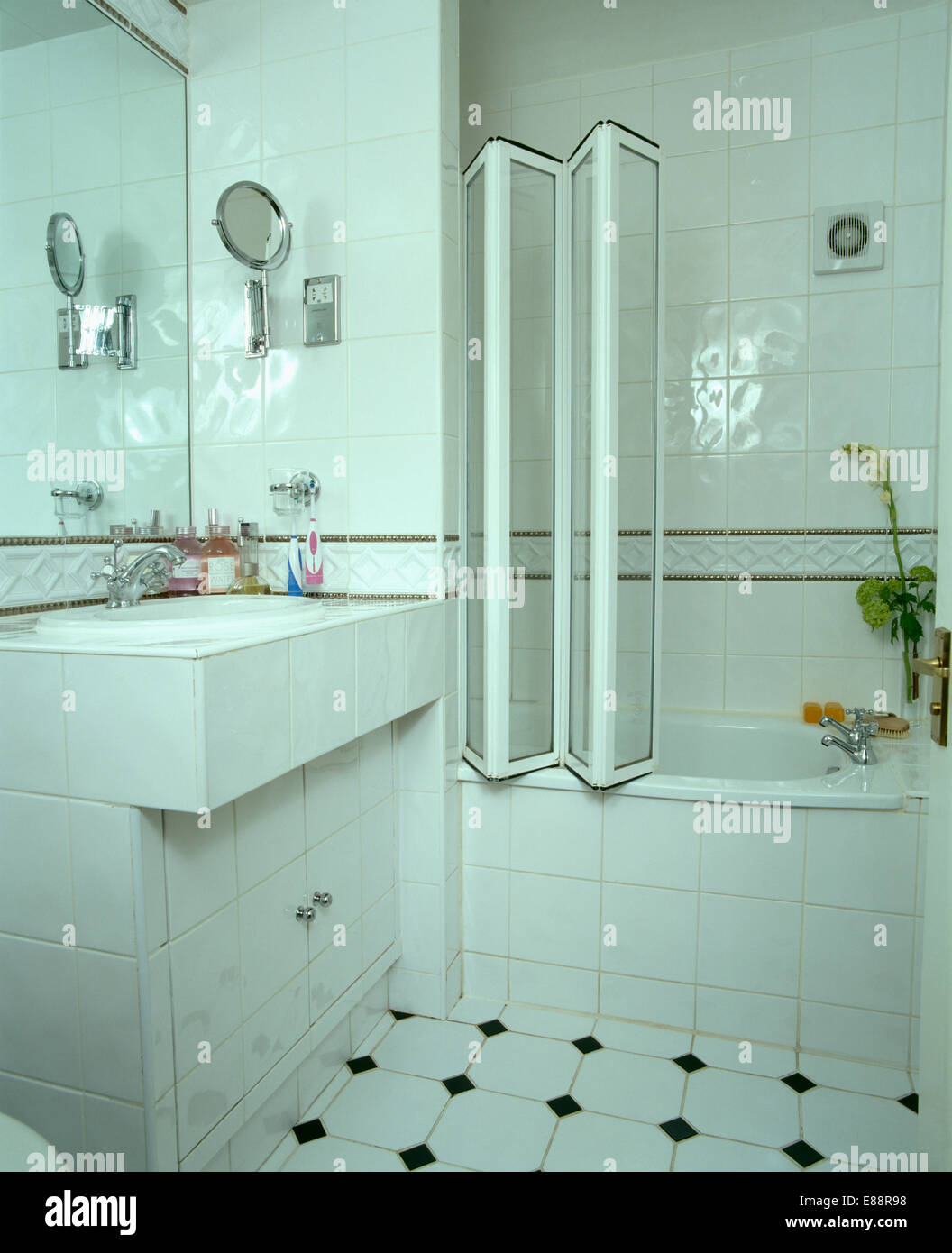 Portes de douche en verre escamotable sur baignoire dans salle de bains carrelée moderne blanc Banque D'Images