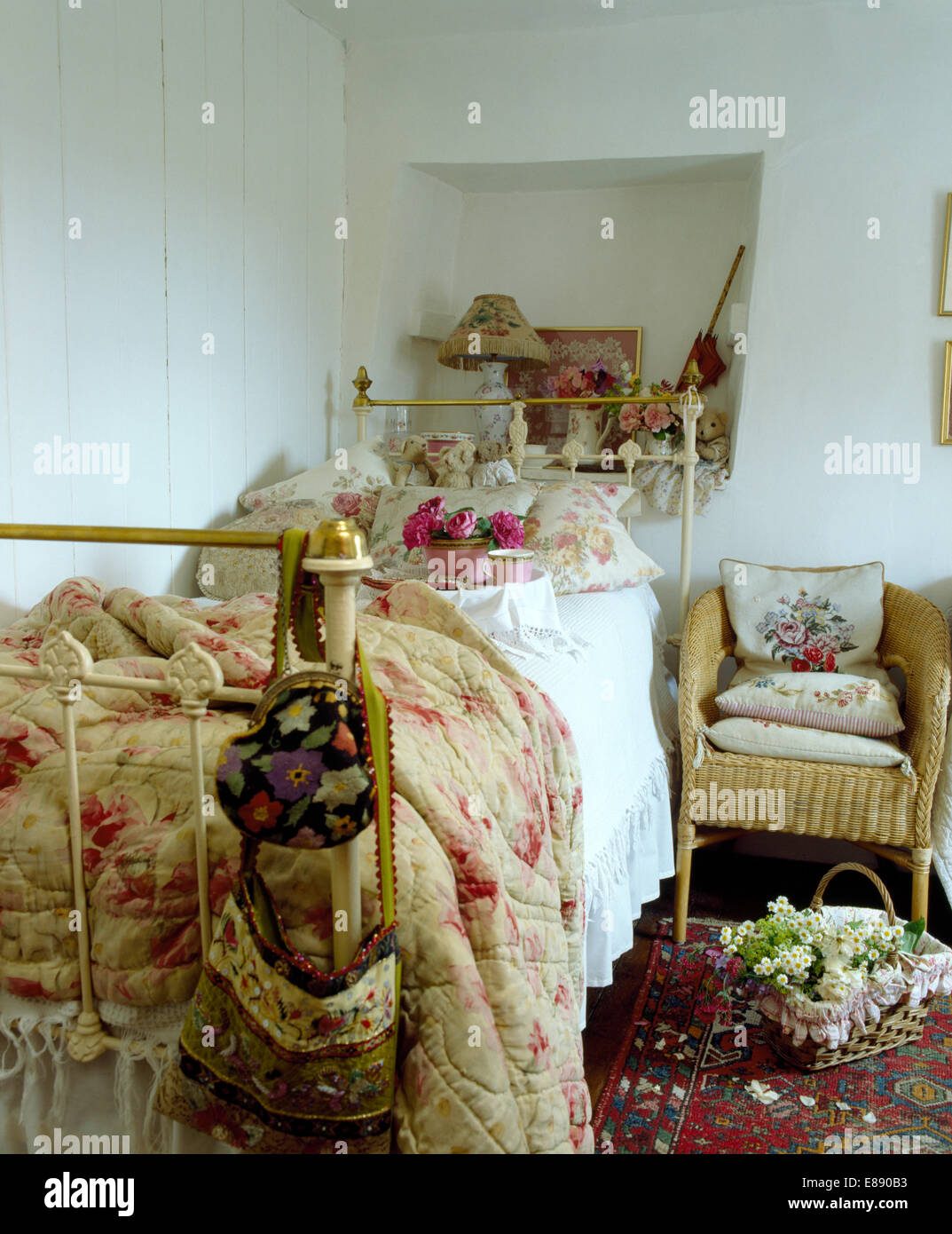 Ancienne courtepointe à motifs de roses et de fleurs coussins sur un lit en fer forgé en chambre cottage Banque D'Images
