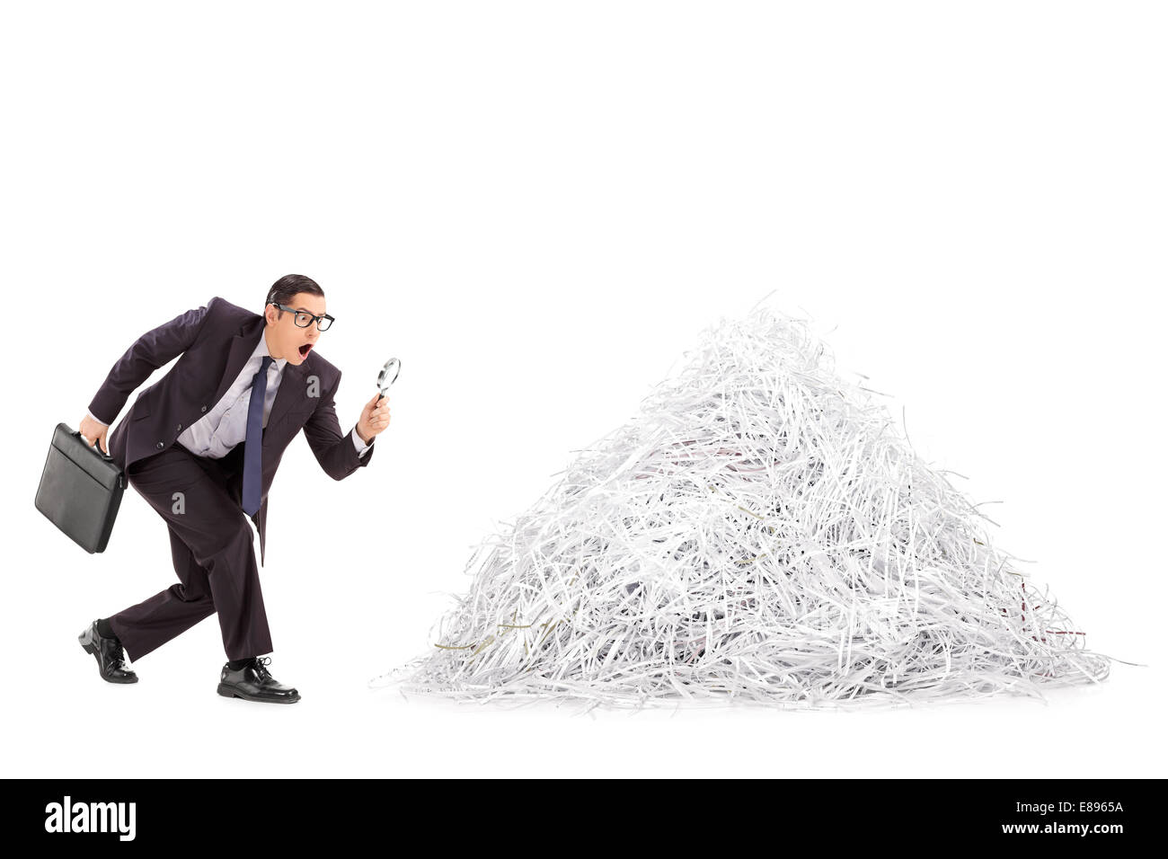 Businessman examining une pile de papier déchiqueté à travers une loupe isolé sur fond blanc Banque D'Images