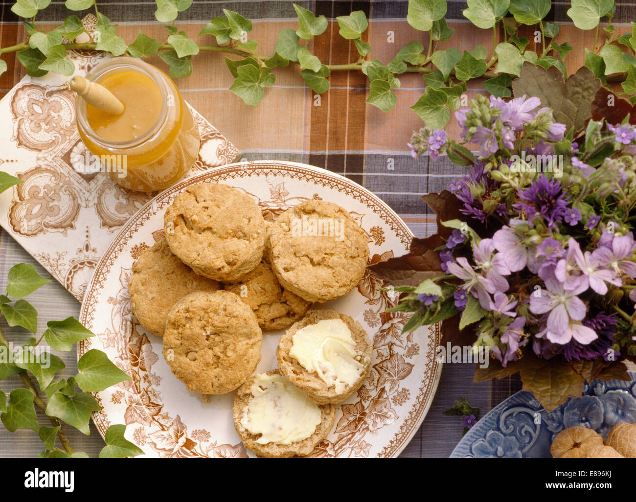 Close-up of plate of scones sur table avec pot de miel et vase de fleurs d'été mauve Banque D'Images