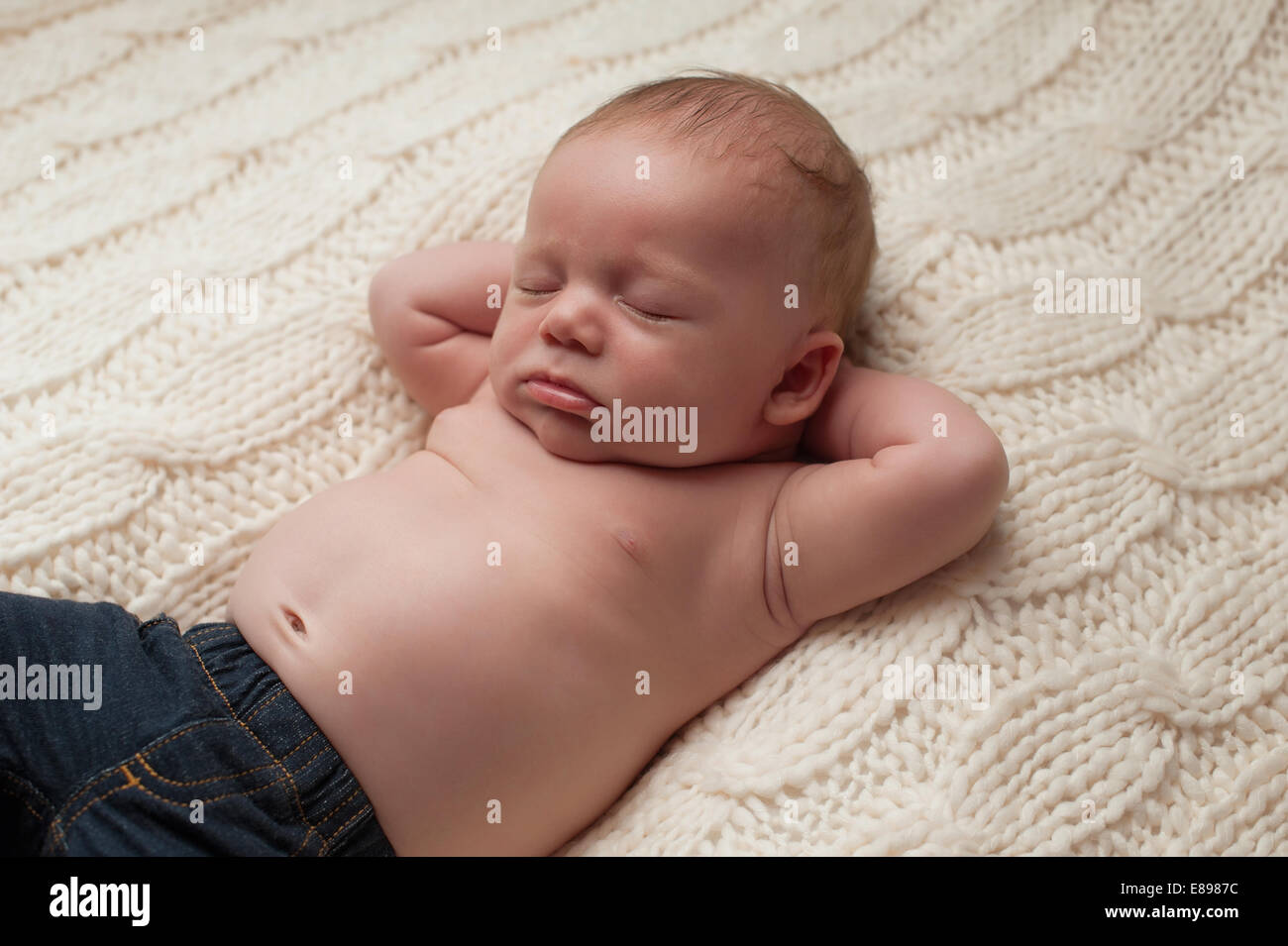 Portrait d'un nouveau-né âgé de 1 mois bébé garçon portant des jeans. Il  est en train de dormir sur son dos une couverture beige avec ses mains  derrière son h Photo Stock -