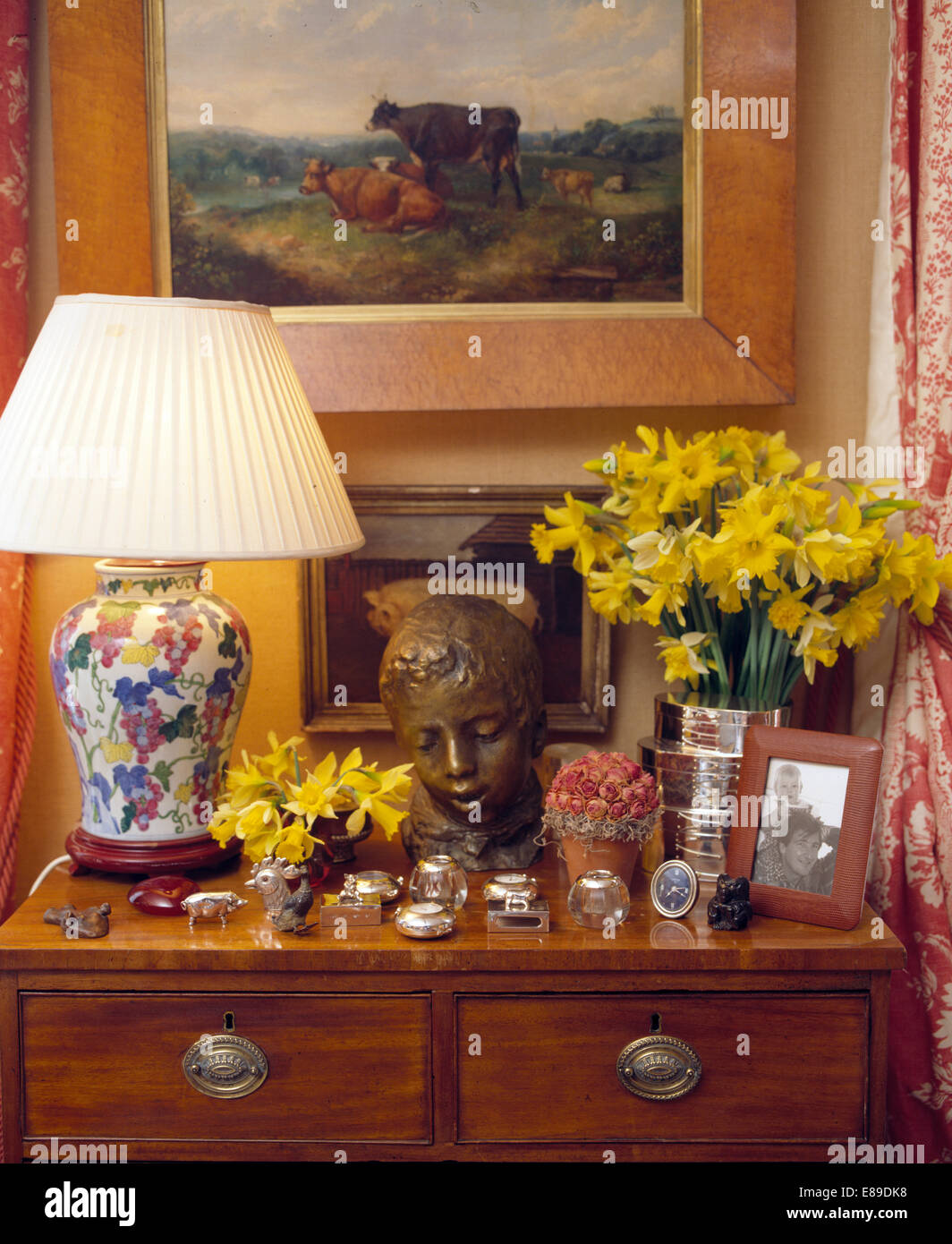 Peinture sur mur au-dessus de la poitrine de tiroirs avec la lampe allumée et tête en bronze avec vase de jonquilles Banque D'Images